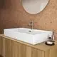 Waschtisch in Seidenweiß von Ideal Standard, rechteckig, mit einem Wasserhahn und Seifenspender auf einer Holzablage, vor einer Korkwand.